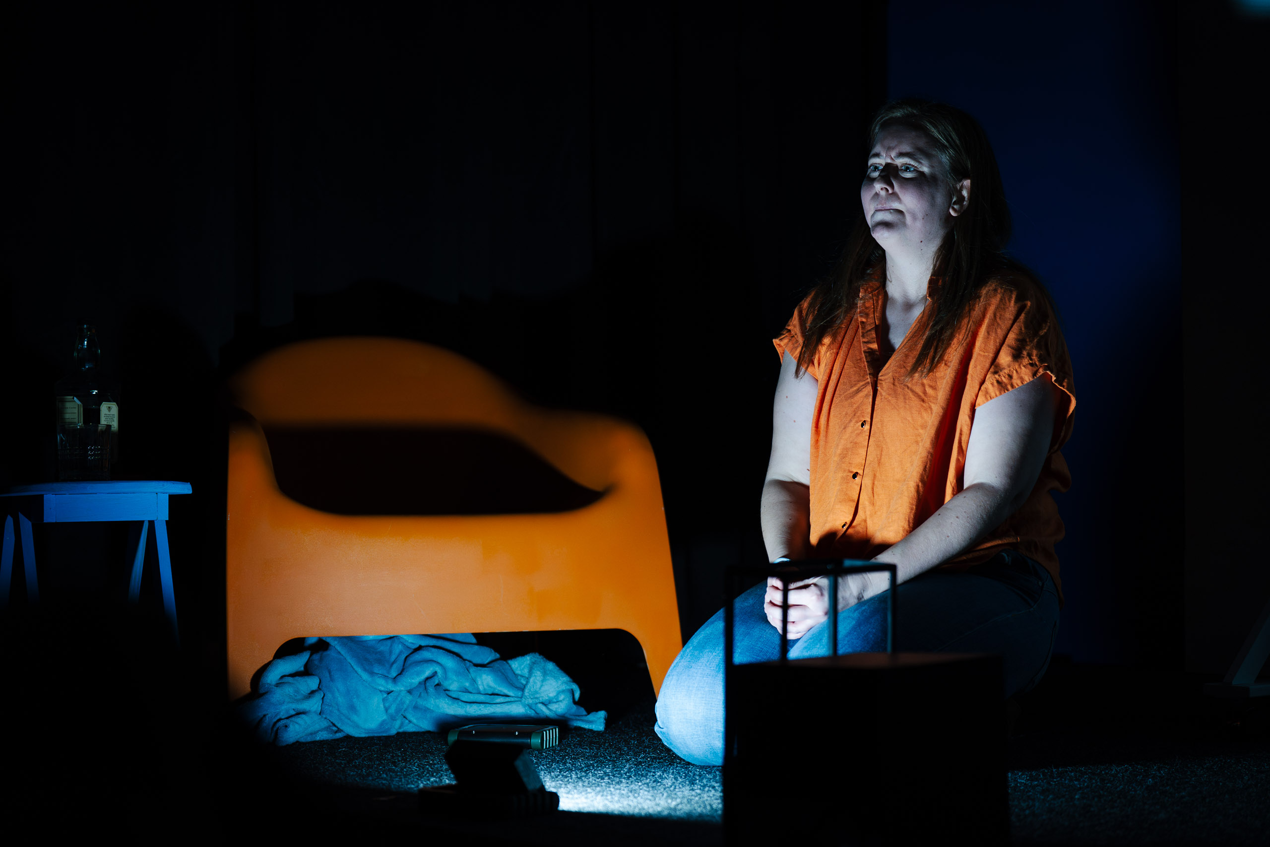 A woman kneels in a dark room, illuminated by a spotlight, with