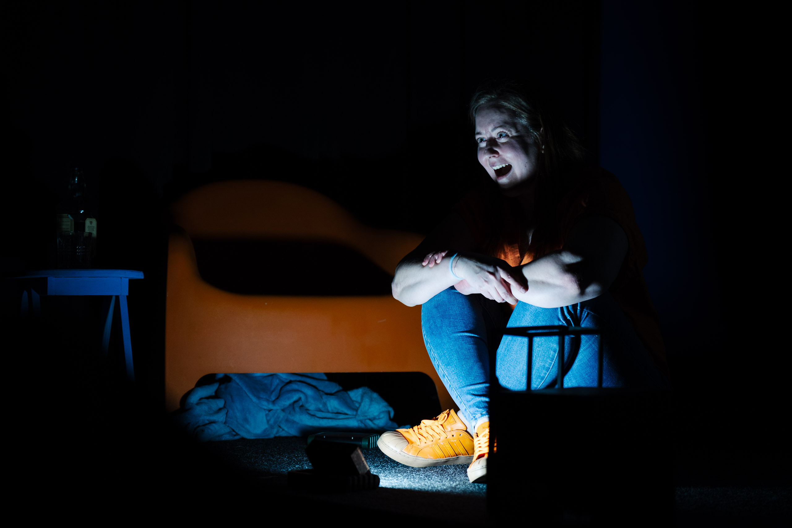 A woman sits on the floor in a dark room, looking distressed and